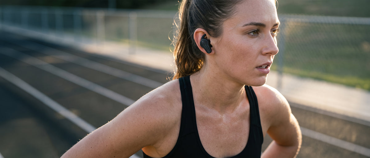 Woman on an outdoor running track wearing black BlueAnt Pump Air X3 sport earbuds