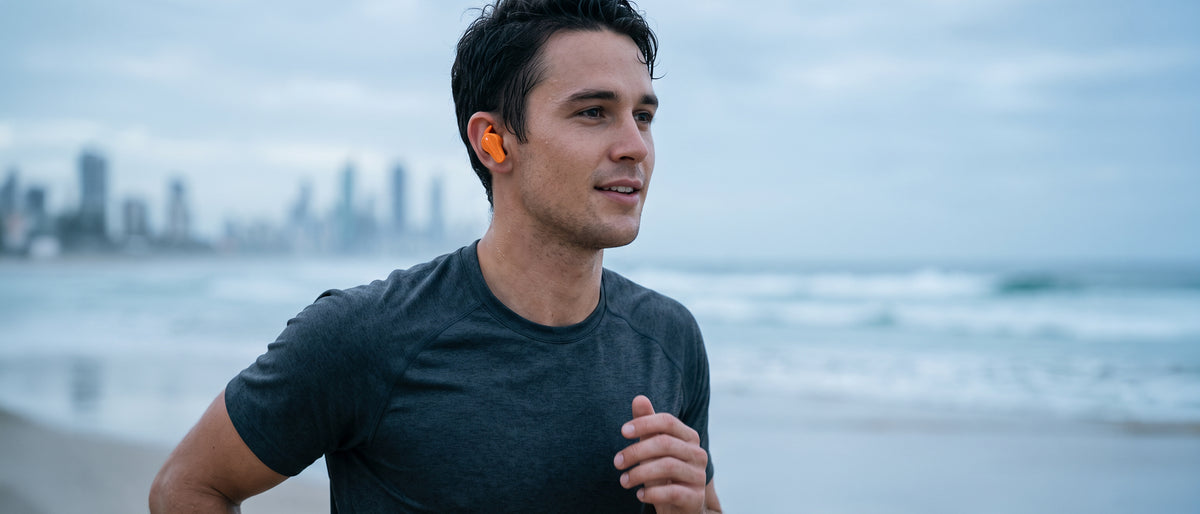 Man running on the beach wearing orange BlueAnt Pump Air X3 earbuds