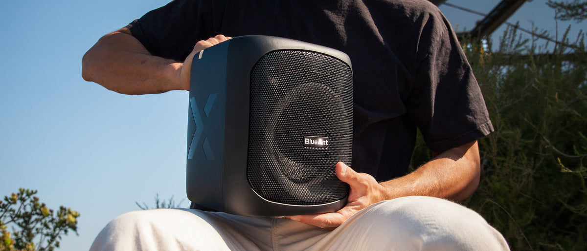 Man carrying the BlueAnt X4 speaker to an outdoor gathering, low angle against the sky